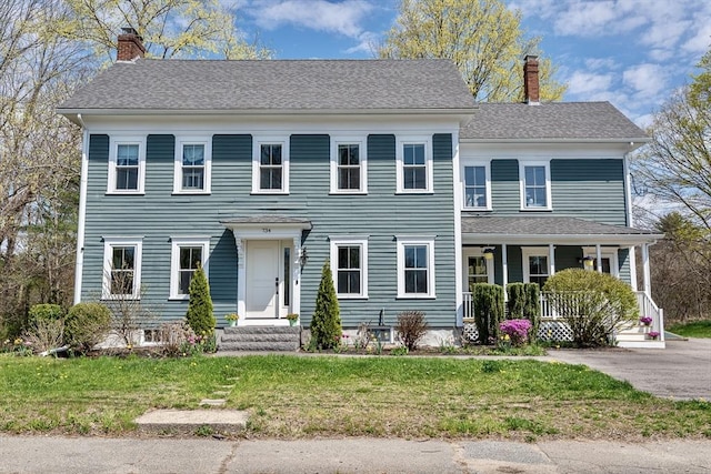colonial inspired home with a chimney, covered porch, and a front yard