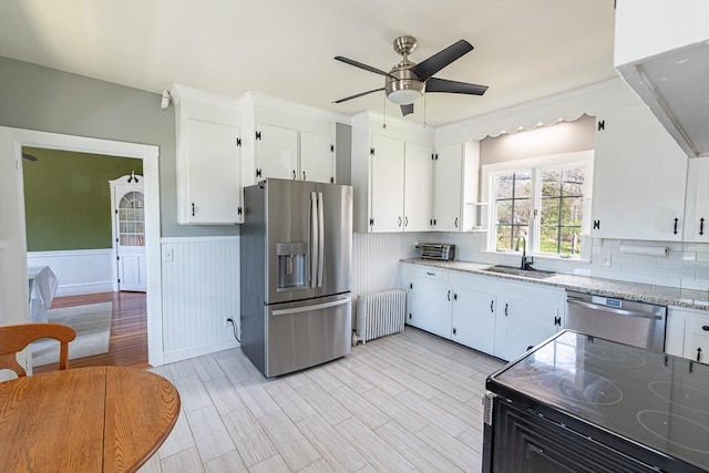 kitchen featuring appliances with stainless steel finishes, white cabinets, radiator, ceiling fan, and a sink