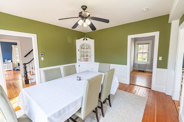 dining room featuring radiator, a wainscoted wall, a ceiling fan, and wood-type flooring