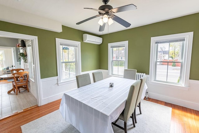 dining space featuring wood finished floors, ceiling fan, an AC wall unit, and baseboards