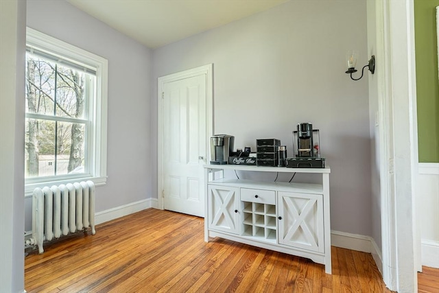 bar featuring wood finished floors, baseboards, and radiator