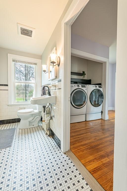 washroom featuring tile walls, a sink, washer and clothes dryer, laundry area, and visible vents