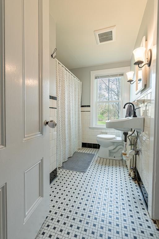 full bath featuring wainscoting, tile walls, a shower with shower curtain, toilet, and visible vents