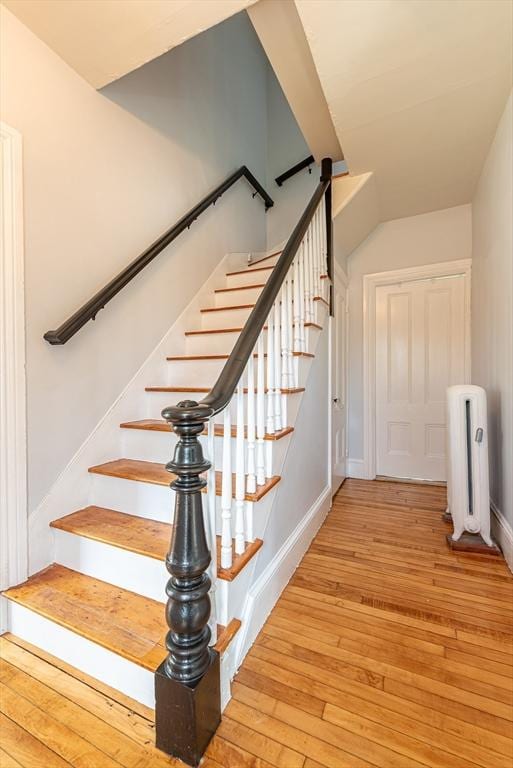 staircase featuring hardwood / wood-style floors, radiator heating unit, vaulted ceiling, and baseboards