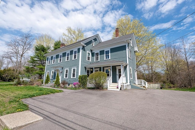 view of front facade featuring a chimney, a porch, aphalt driveway, and a front yard
