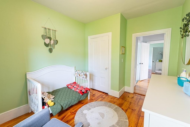 bedroom featuring light wood finished floors, a crib, and baseboards