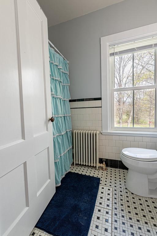 full bath with a shower with curtain, tile walls, radiator, a wainscoted wall, and toilet