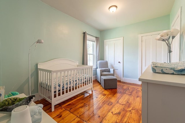 bedroom with light wood finished floors, a nursery area, and baseboards