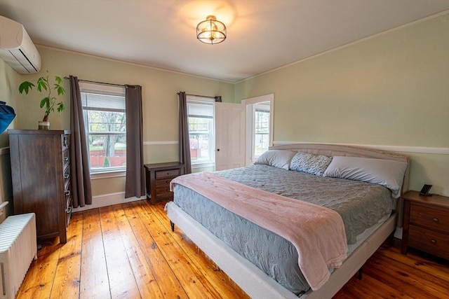 bedroom with baseboards, radiator, light wood-type flooring, ornamental molding, and a wall mounted air conditioner