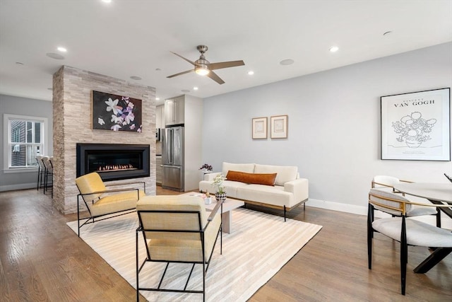 living room with ceiling fan, a large fireplace, and light hardwood / wood-style floors