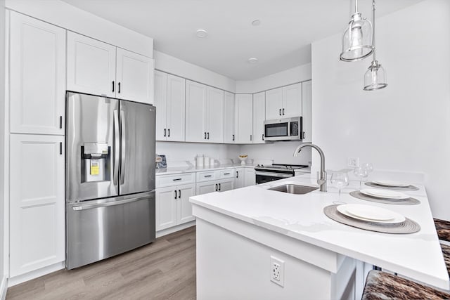 kitchen featuring pendant lighting, sink, white cabinetry, stainless steel appliances, and light wood-type flooring