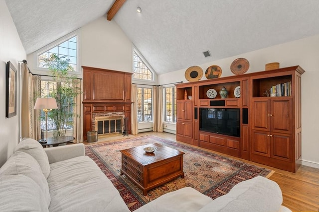 living room with beam ceiling, high vaulted ceiling, a textured ceiling, a brick fireplace, and light wood-type flooring