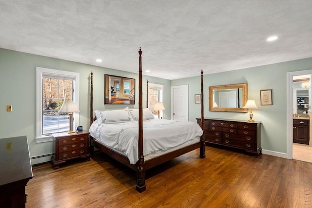 bedroom featuring multiple windows, a baseboard heating unit, hardwood / wood-style flooring, and connected bathroom