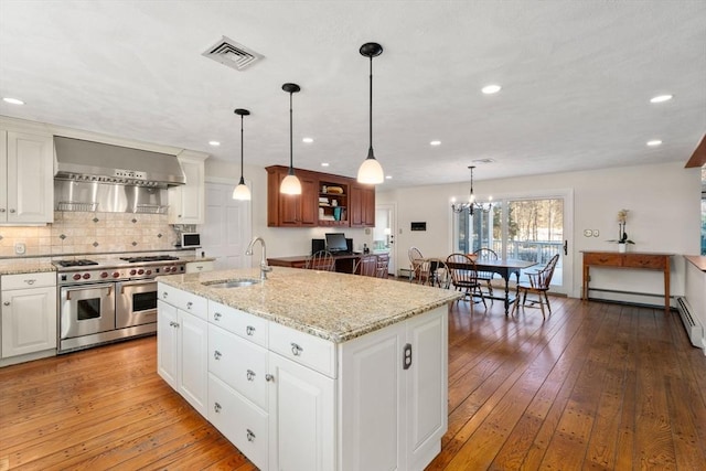 kitchen with sink, hanging light fixtures, range with two ovens, and a center island with sink