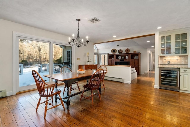 dining room with bar area, a chandelier, hardwood / wood-style flooring, beverage cooler, and a baseboard heating unit