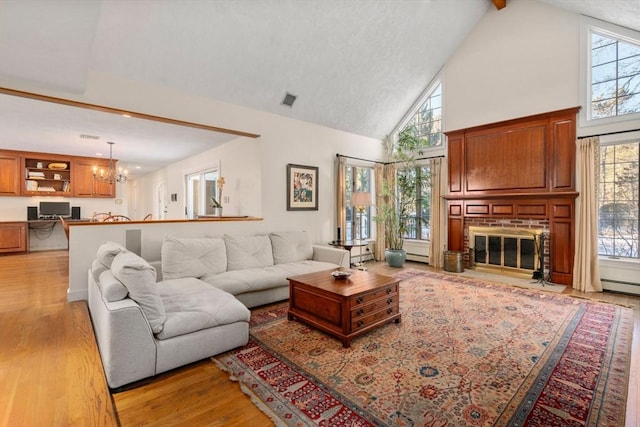 living room with baseboard heating, an inviting chandelier, high vaulted ceiling, a fireplace, and light wood-type flooring