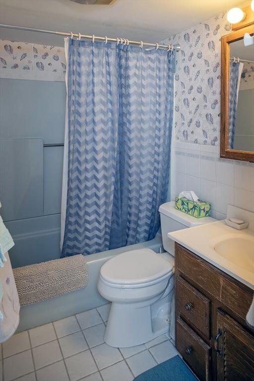 full bathroom featuring wallpapered walls, shower / bath combo with shower curtain, wainscoting, tile patterned floors, and tile walls