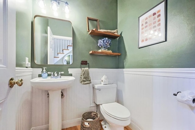 bathroom with a sink, a wainscoted wall, toilet, and wood finished floors