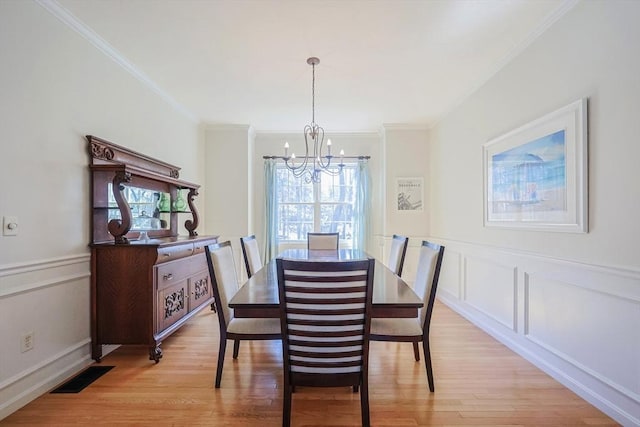 dining room with visible vents, crown molding, wainscoting, a chandelier, and light wood finished floors