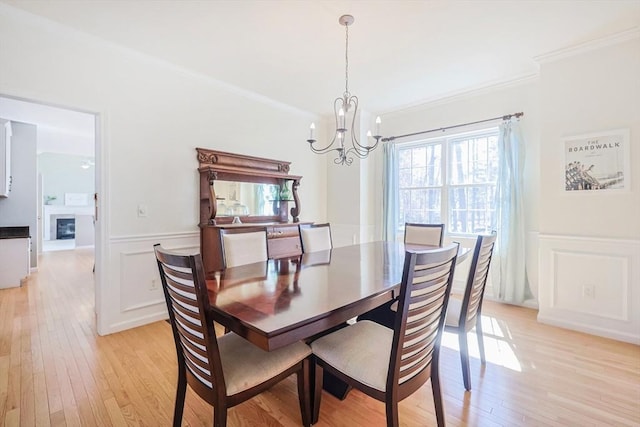 dining room featuring crown molding, a decorative wall, a wainscoted wall, a chandelier, and light wood-style flooring