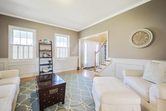 living room featuring wood finished floors, crown molding, a decorative wall, and a wainscoted wall