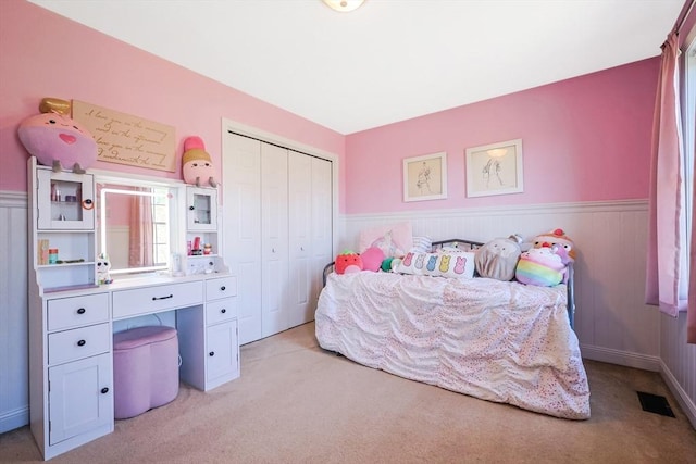 bedroom featuring a closet, wainscoting, and light colored carpet