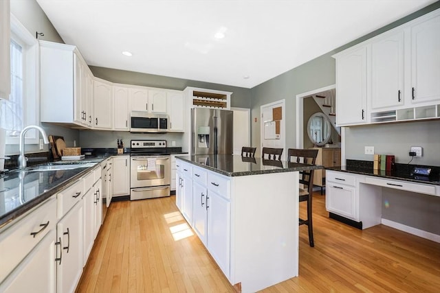 kitchen with a kitchen breakfast bar, appliances with stainless steel finishes, a sink, light wood-style floors, and white cabinetry