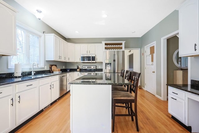 kitchen with appliances with stainless steel finishes, light wood-type flooring, a sink, white cabinets, and a breakfast bar