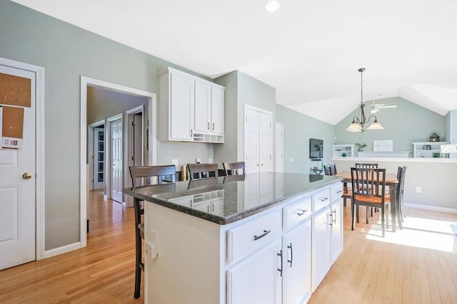 kitchen featuring pendant lighting, a kitchen bar, dark stone counters, white cabinetry, and light wood finished floors