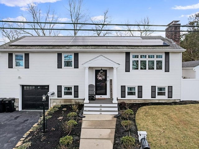 bi-level home featuring a garage, a front lawn, and solar panels