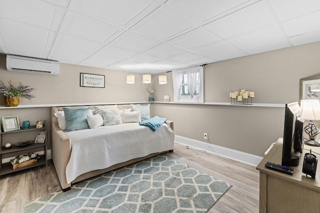 bedroom with a wall mounted air conditioner, a drop ceiling, and light hardwood / wood-style flooring