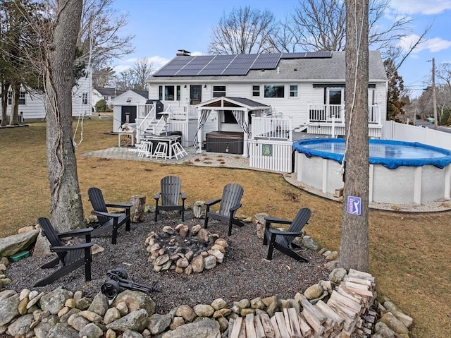 rear view of property with a patio, a pool side deck, an outdoor fire pit, a gazebo, and solar panels