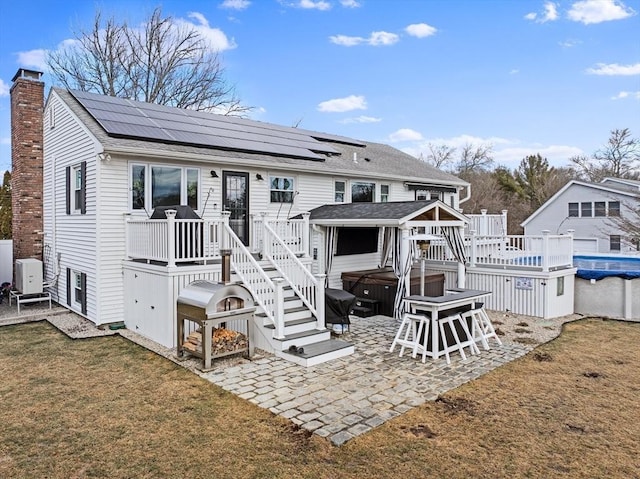 rear view of house featuring a hot tub, a patio, a deck, and solar panels