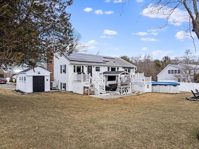 rear view of house featuring a pool side deck, a lawn, solar panels, and a storage shed