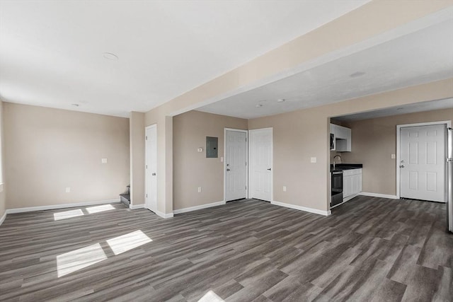 unfurnished living room featuring baseboards, dark wood finished floors, stairway, electric panel, and a sink