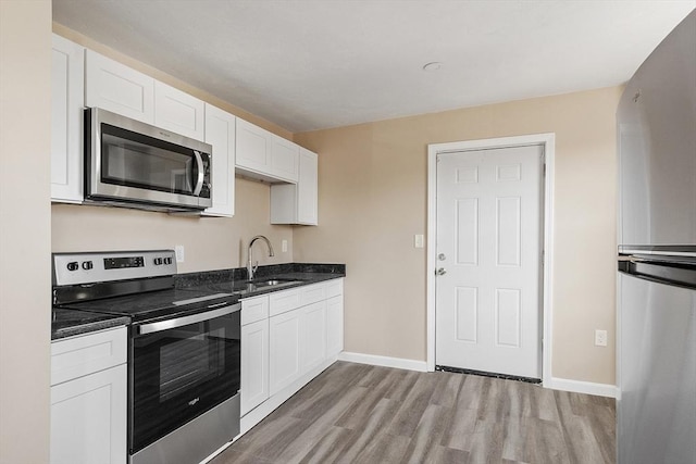 kitchen with baseboards, light wood-style flooring, appliances with stainless steel finishes, white cabinets, and a sink