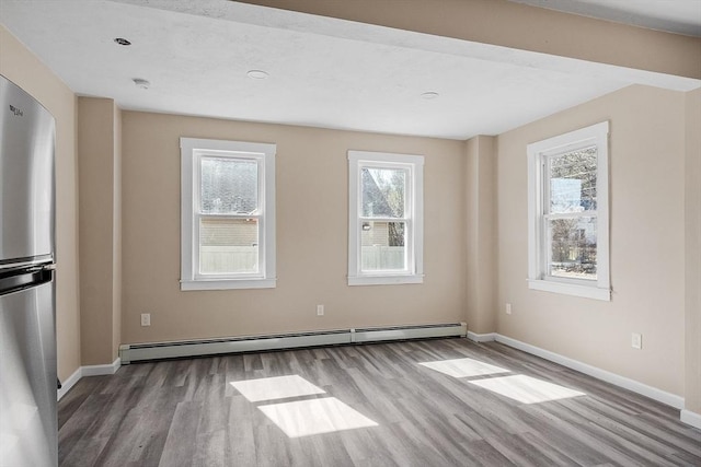 spare room with a baseboard heating unit, wood finished floors, and baseboards