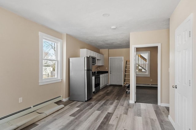 kitchen with light wood-style flooring, a baseboard heating unit, white cabinetry, appliances with stainless steel finishes, and baseboard heating