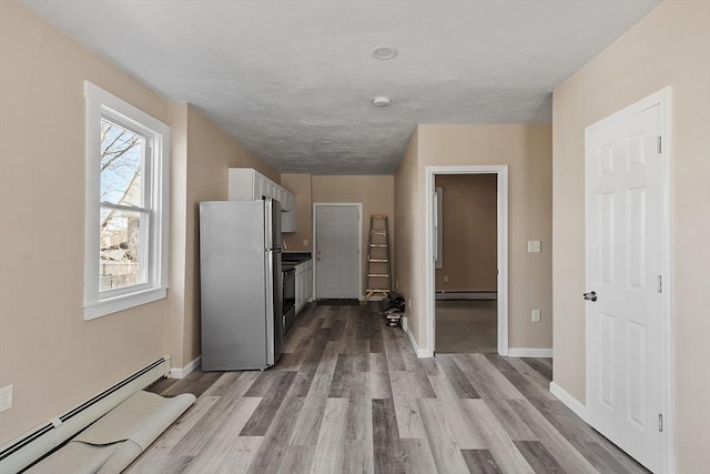 kitchen featuring baseboards, baseboard heating, light wood-style flooring, freestanding refrigerator, and a baseboard radiator