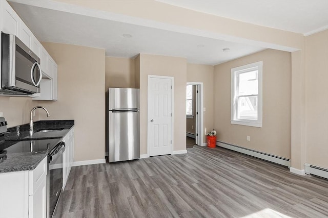 kitchen featuring light wood finished floors, appliances with stainless steel finishes, a baseboard heating unit, and a sink