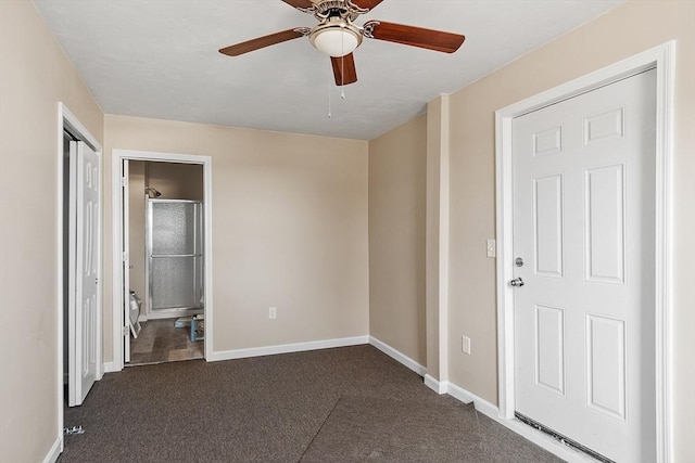 unfurnished bedroom with dark carpet, ensuite bath, baseboards, and ceiling fan