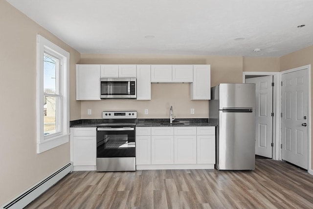 kitchen featuring baseboard heating, light wood finished floors, appliances with stainless steel finishes, and a sink