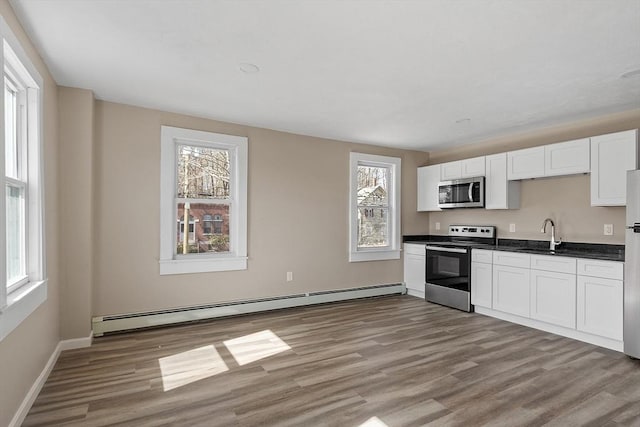 kitchen with dark countertops, light wood finished floors, stainless steel microwave, a baseboard heating unit, and electric range