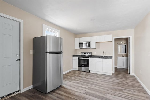 kitchen featuring a sink, dark countertops, white cabinetry, stainless steel appliances, and light wood finished floors