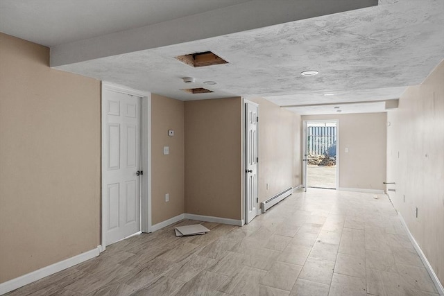 empty room featuring baseboard heating, a textured ceiling, attic access, and baseboards