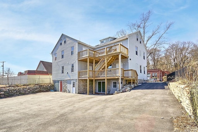 rear view of property featuring a deck, stone siding, and driveway