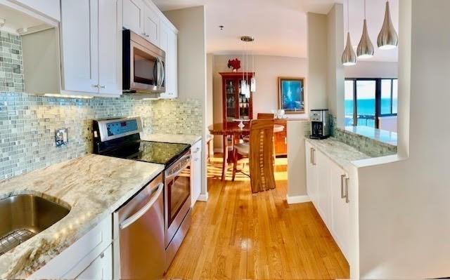 kitchen featuring white cabinets, hanging light fixtures, light wood-type flooring, appliances with stainless steel finishes, and light stone counters