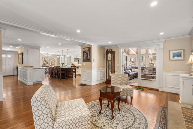 living room with light wood-style floors, ornamental molding, a decorative wall, and recessed lighting