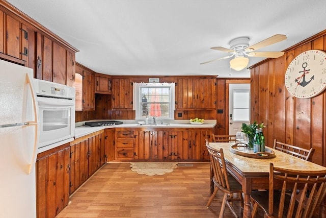 kitchen with white appliances, wood walls, ceiling fan, and light wood-type flooring