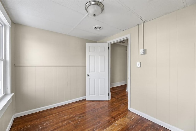 empty room with dark hardwood / wood-style flooring, a drop ceiling, and wooden walls